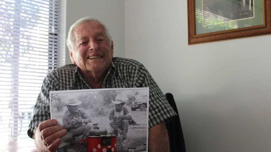 Jimmy Hayes with and old photo at the stock camp in the 1970s, with the same red mug.