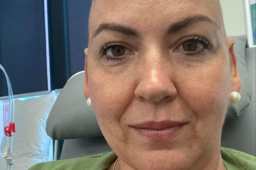A bald woman sitting in a hospital chair.