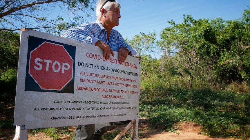 A grey-haired man in a white and blue shirt stands at Ardyaloon entrance in front ogf a sign that reads "Stop"