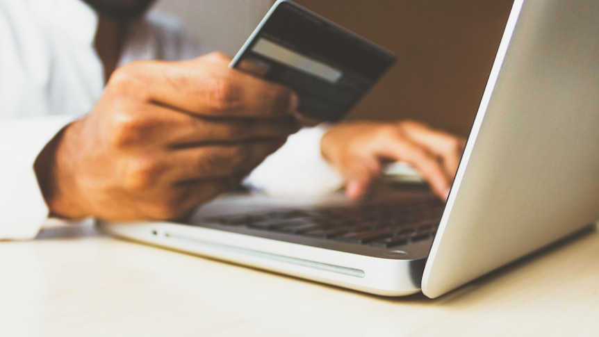 A stock photo showing a laptop close-up and the hands of a person using a credit card