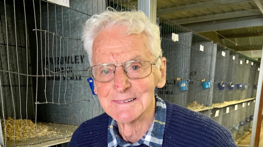 A man holding a white chicken with cage lined up behind him