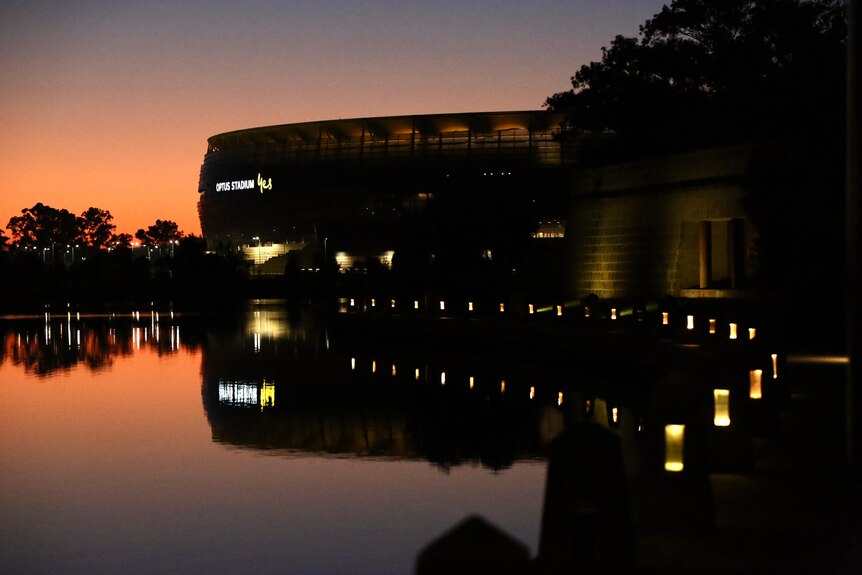 Dawn begins to appear with an orange hue over the Perth Stadium reflected onto the Swan River.