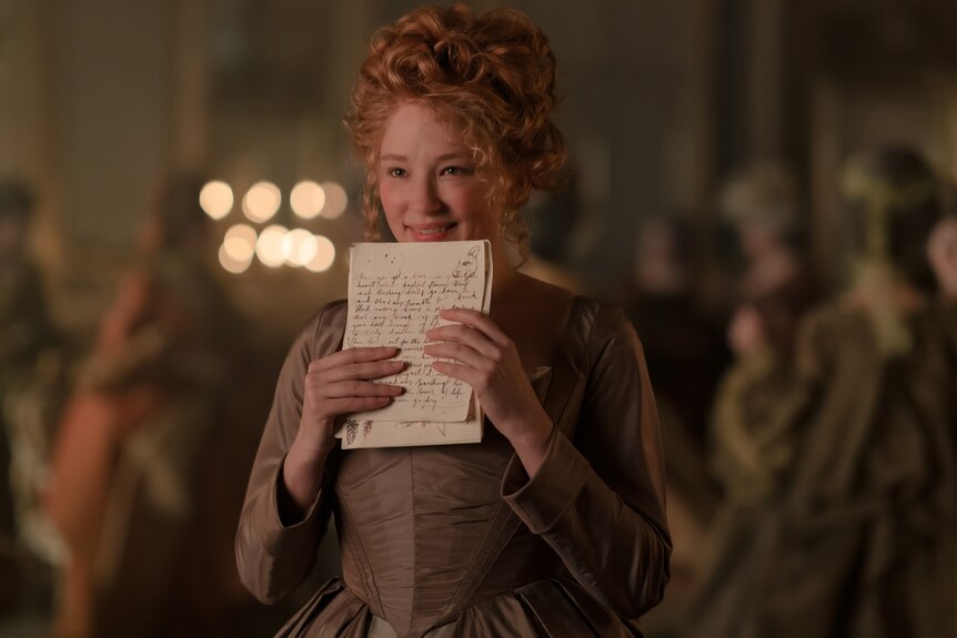 A 30-something woman smiles widely as she holds the pages of a letter written in cursive to his face