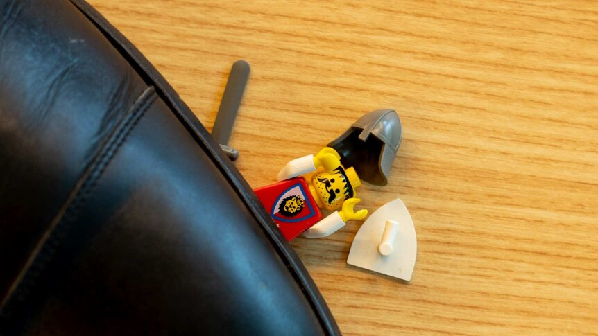 A Lego figure lies on the ground, squashed by a man's shoe.