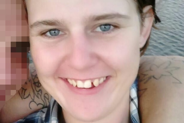 A head and shoulders shot of a smiling young woman with a man's tattooed arm around her shoulders.