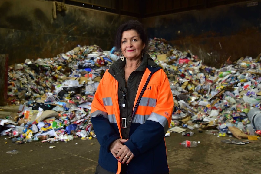 A woman, wearing a high-viz jacket stands in front of recycling waste