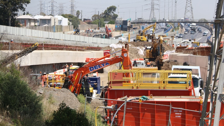 A number of earthmoving machines work alongside a busy highway.