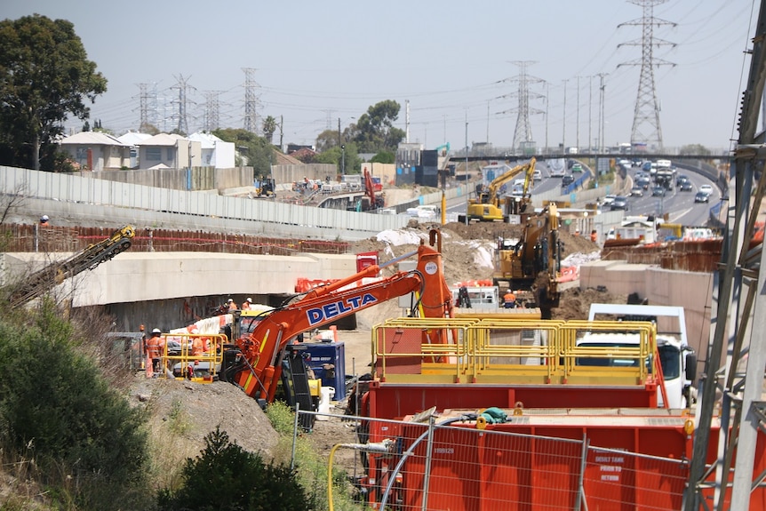 A number of earthmoving machines work alongside a busy highway.