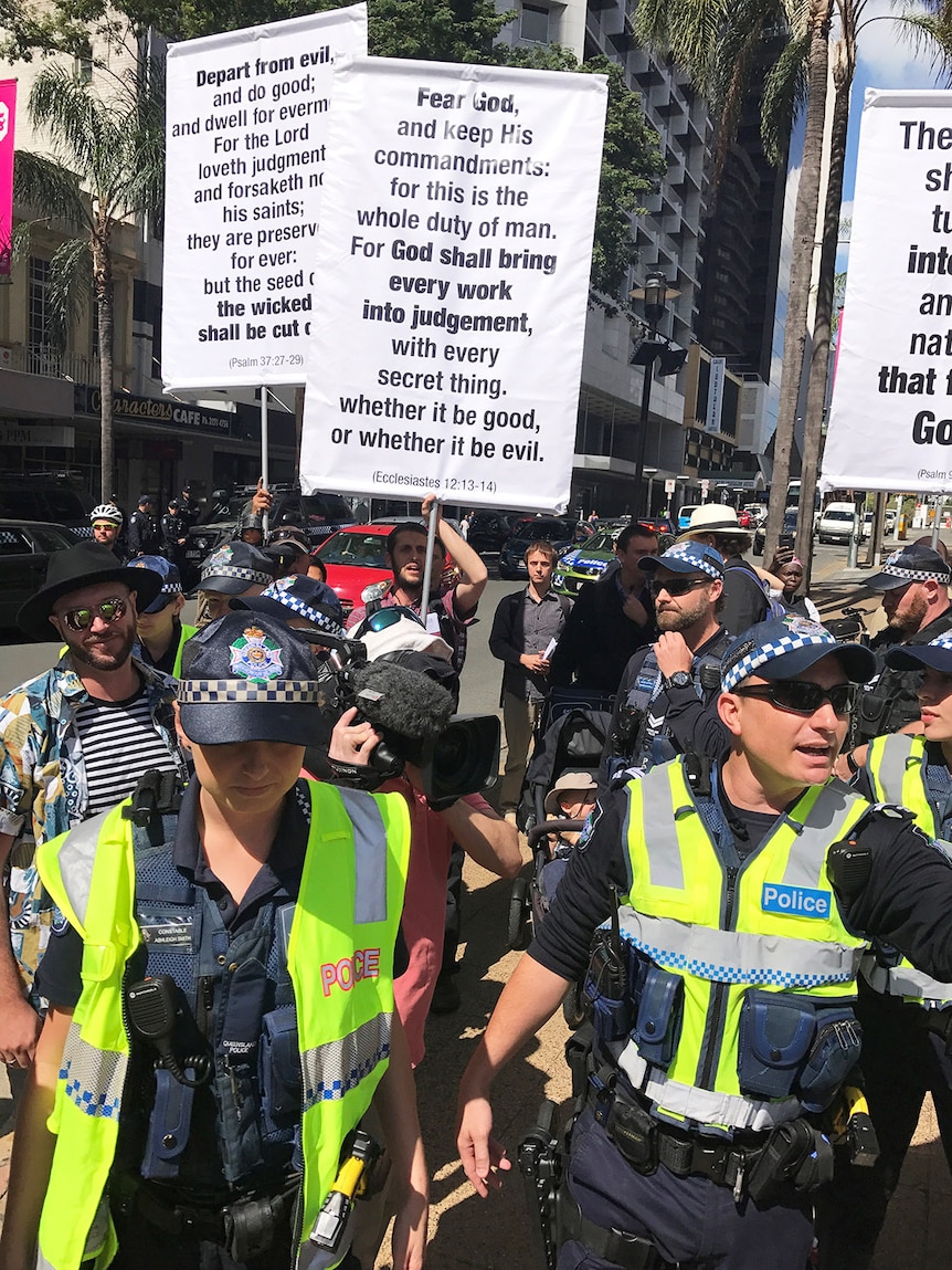 Protesters hold placards with verses from the Bible, surrounded by police, at the Brisbane rally for same-sex marriage.