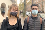 A young woman and man in facemasks pose for the camera in a Paris street.