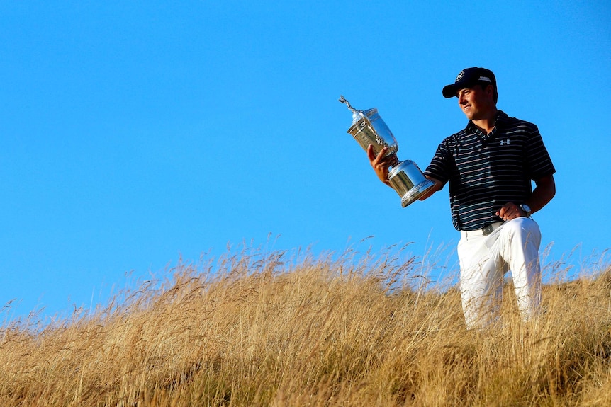 Jordan Spieth, with a bright blue sky behind him, looks at the US Open trophy.