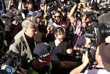 Pell surrounded by police and crowd of camera crews and photographers.