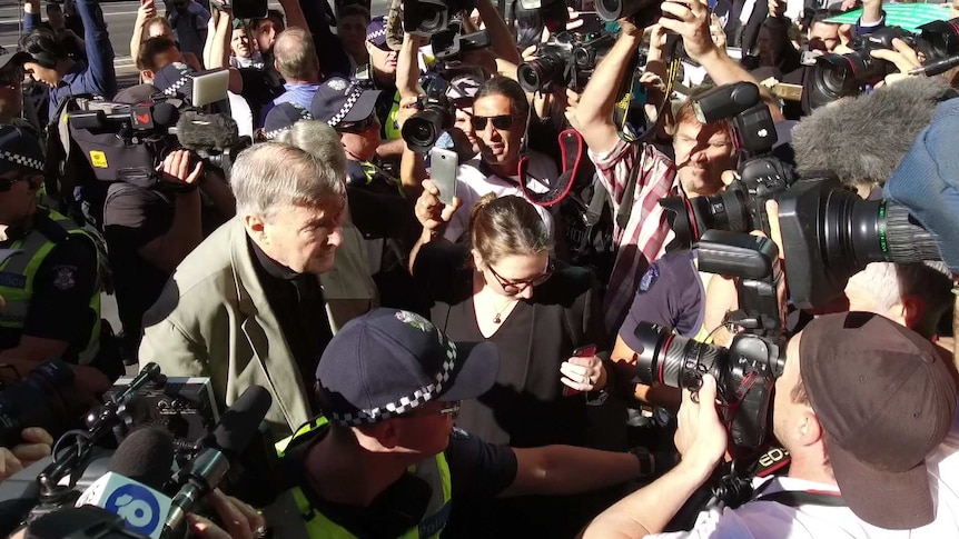 Pell surrounded by police and crowd of camera crews and photographers.