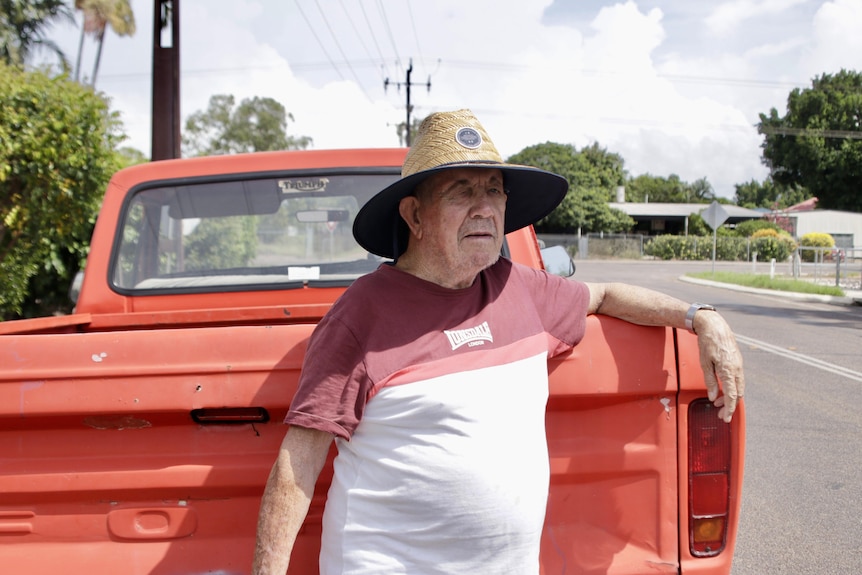 A man wears a hat in front of a red pick up truck. 