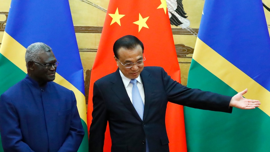 Solomon Islands Prime Ministeer and Chinese Premier stand in front of their nations flags. 