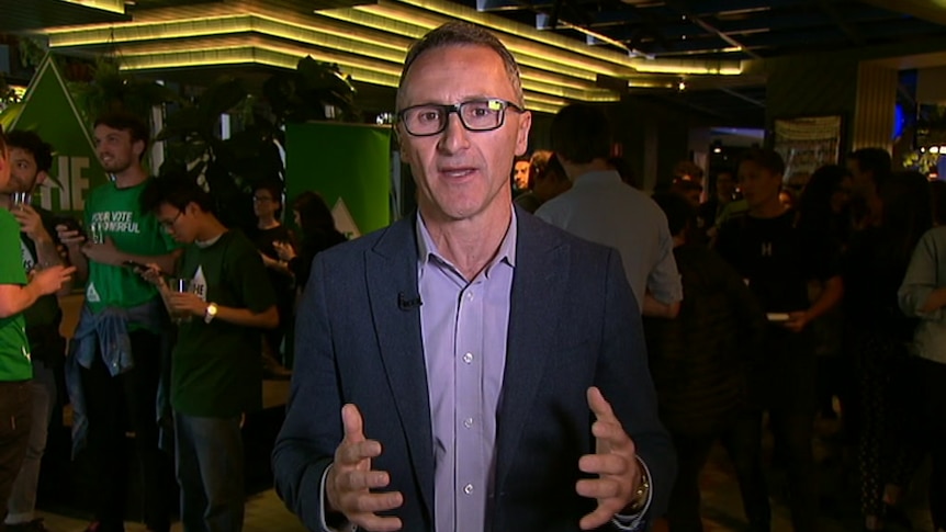 Richard Di Natale speaks to the camera in front of a Greens party function.