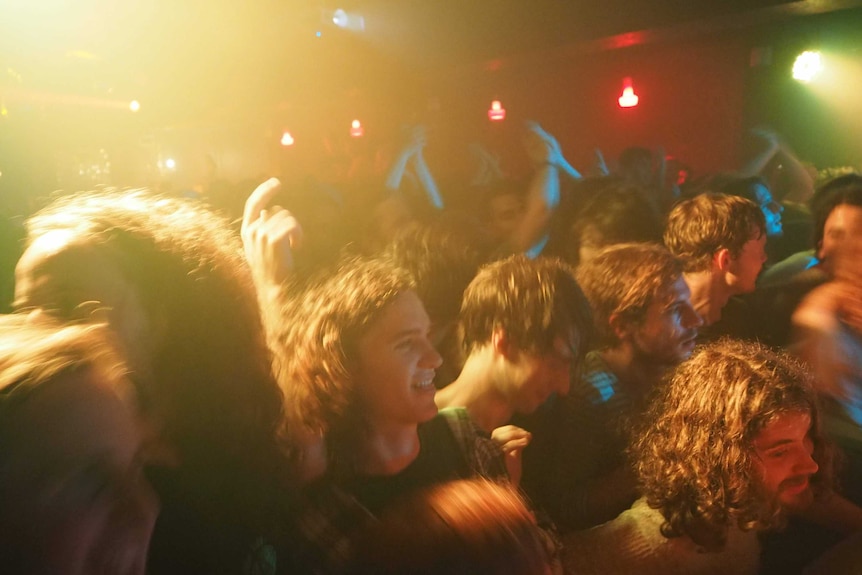 A picture of a bandroom with a crowd packed in tight, dancing under yellow and red and green lights.