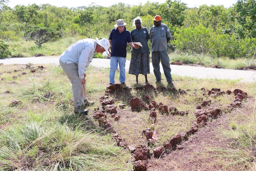 Professor Campbell Macknight bends over to examine an arrangement of rocks on the ground.