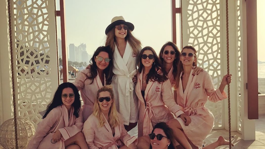 An image showing a group of eight women wearing matching robes and sunglasses at a hotel in Dubai