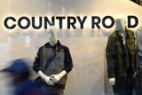 A blurred figure walks past a Country Road storefront, with mannequins in the window.