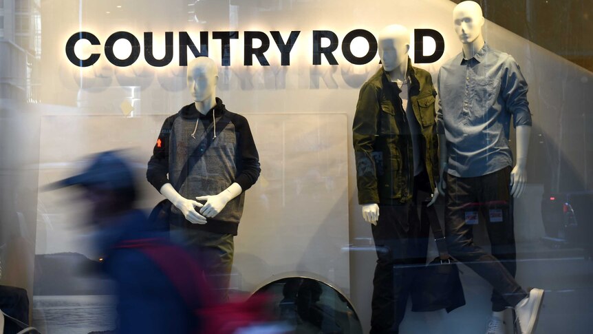 A blurred figure walks past a Country Road storefront, with mannequins in the window.