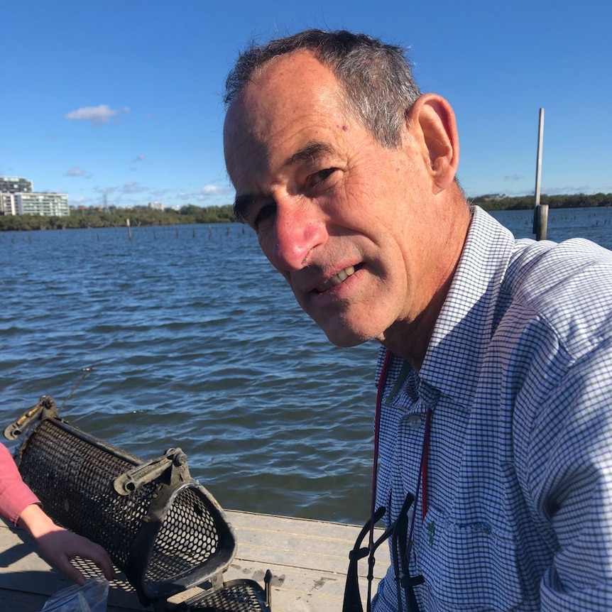 A man in a blue checked shirt sits in a boat on a river.