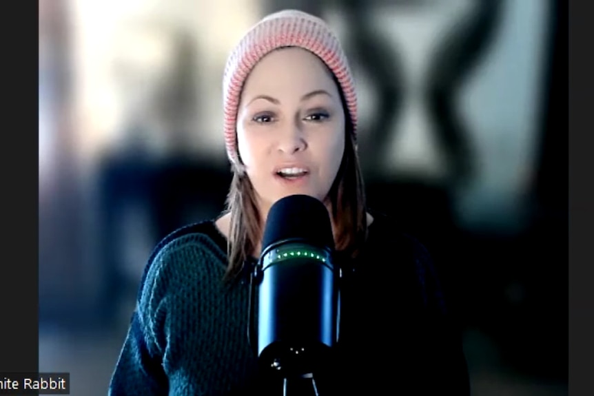 A woman wearing a pink beanie hat sitting behind a microphone with her surroundings blurred out