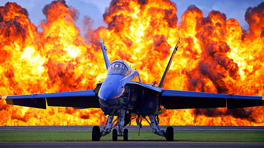 A wall of fire erupts behind a US Navy Blue Angels F/A-18 at the 2012 Kaneohe Bay Air Show.
