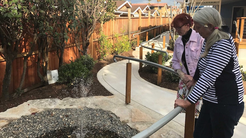 Two women watch a waterfall in a garden.