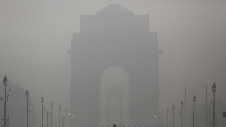 A man rides his bicycle next to Indian soldiers marching in front of India Gate on a smoggy morning in New Delhi.