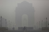 A man rides his bicycle next to Indian soldiers marching in front of India Gate on a smoggy morning in New Delhi.