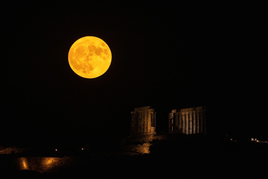 A yellow, full moon rises above a temple at night