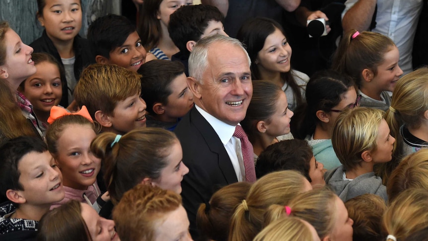 Prime Minister Malcolm Turnbull smiles gleefully sitting among primary aged schoolchildren