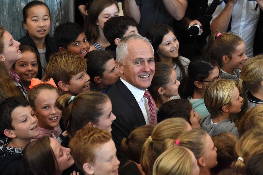 Prime Minister Malcolm Turnbull smiles gleefully sitting among primary aged schoolchildren