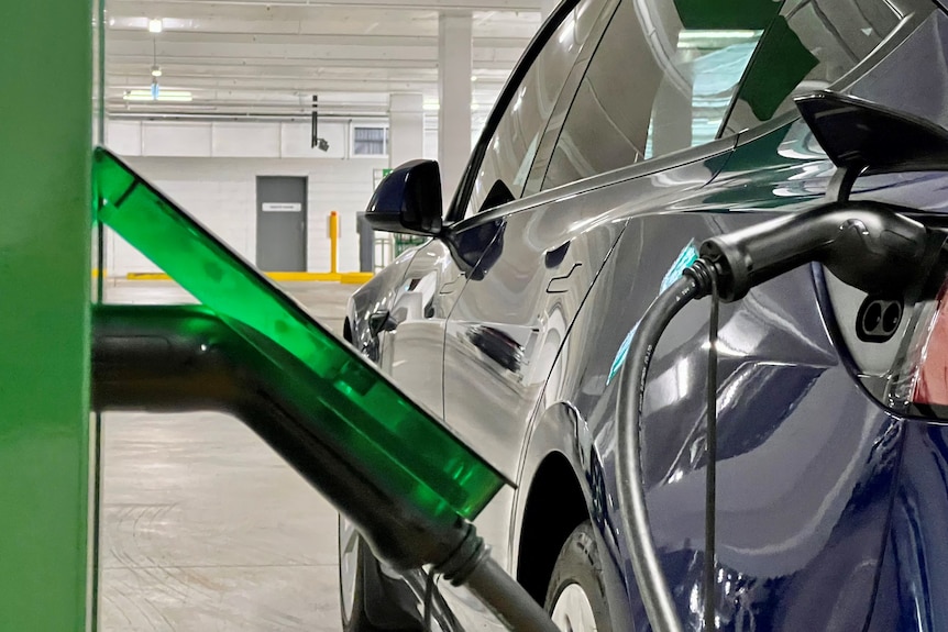 An electric car hooked up to a charger in what appears to be an underground car park.