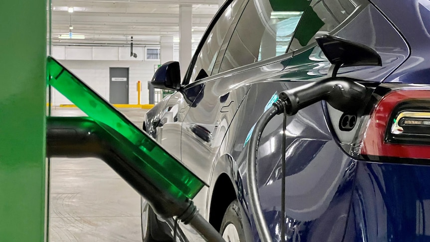 A charging station with cords and a car attached with the woolworths logo on the charging box in green