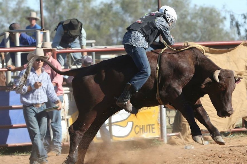 A man holds onto a bull at the Tibooburra Rodeo