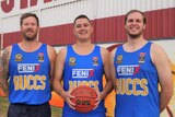 Three basketballers standing holding one ball and smiling out the front of stadium