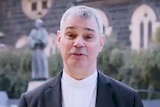Catholic Archbishop of Melbourne Peter Comensoli speaks into the camera with St Patrick's Cathedral in the background.