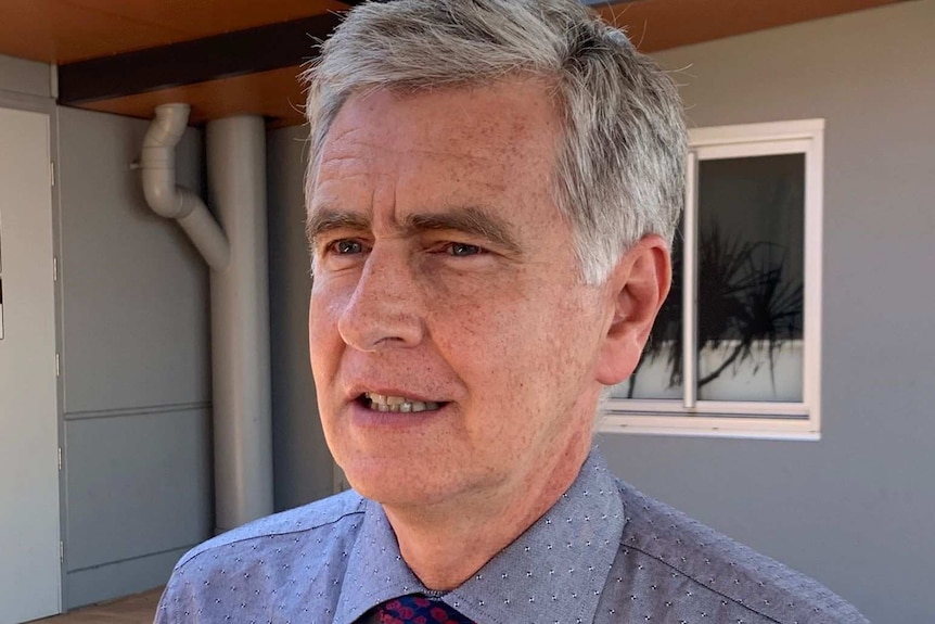 A silver-haired man in a tie standing outside a hospital