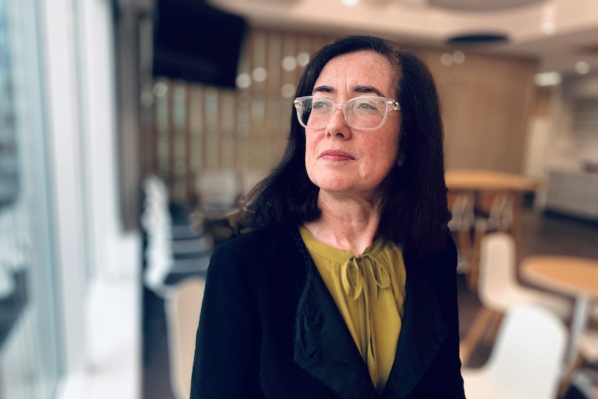 A woman wearing glasses, in a Sydney CBD office building, looking out the window.