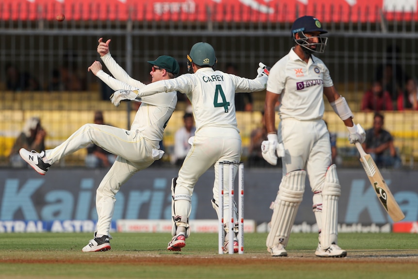 Australia fielders Steve Smith and Alex Carey celebrate removing India's Cheteshwar Pujara, who looks sad in the foreground.