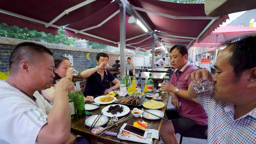 A group of Chinese friends down shots of Baijiu at a barbeque restaurant.
