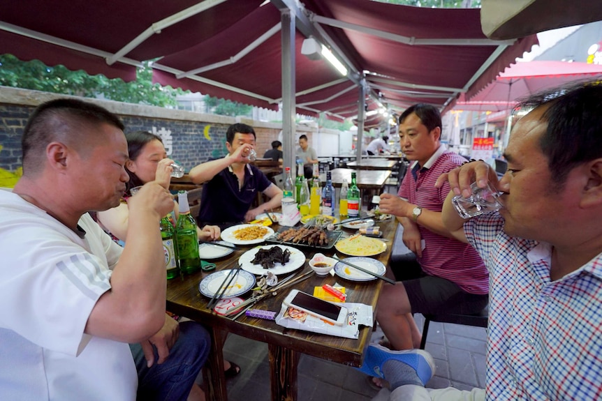 A group of Chinese friends down shots of Baijiu at a barbeque restaurant.