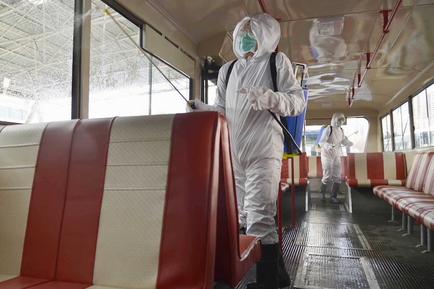 Men in hazmat suits spray liquid over the seats of a bus