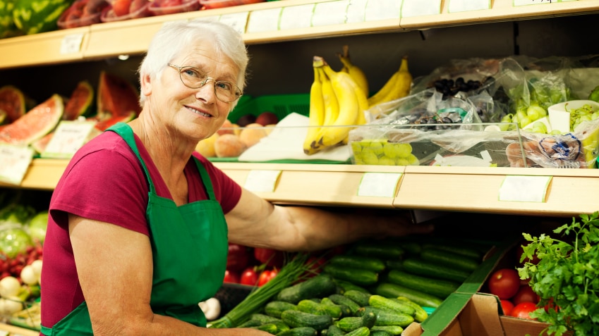 Senior woman arranging vegetables on shelf.