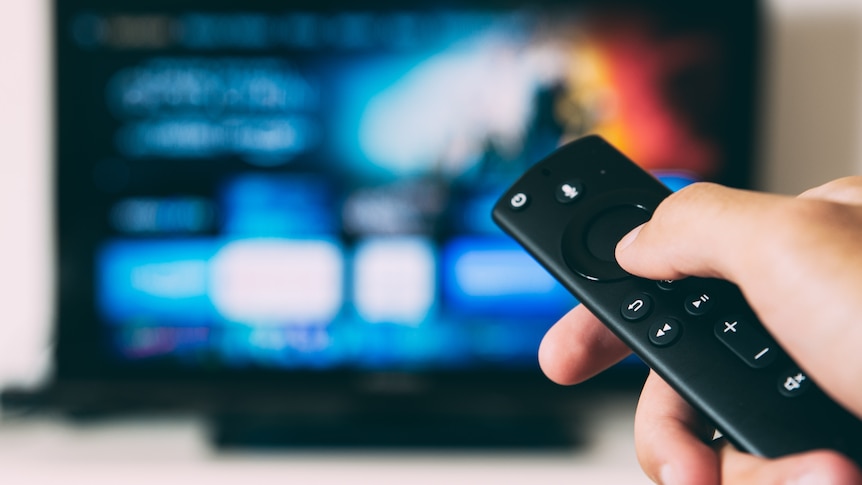 A hand holds a remote pointed towards a large TV.