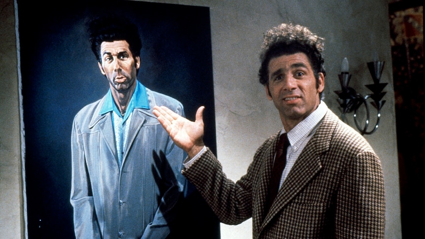 Michael Richards as Kramer pointing to an illustrated portrait of himself