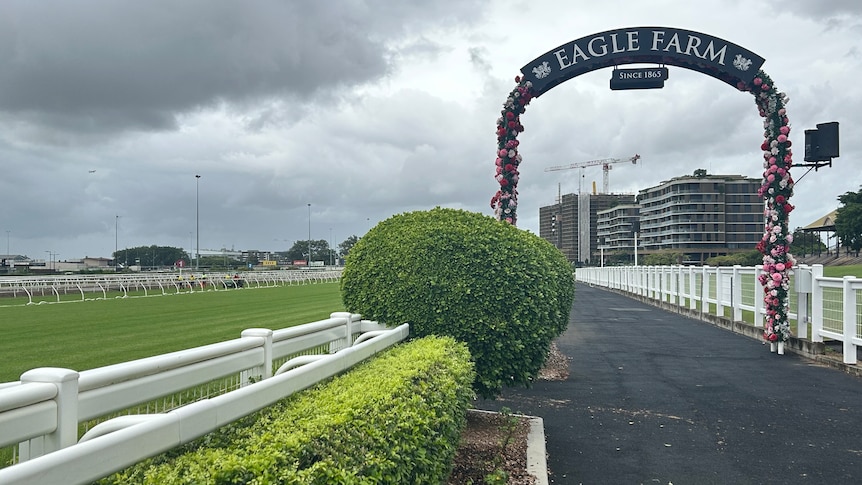 An image of a footpath next to a racecourse with green grass and a sign in the background that says 'Eagle Farm'.