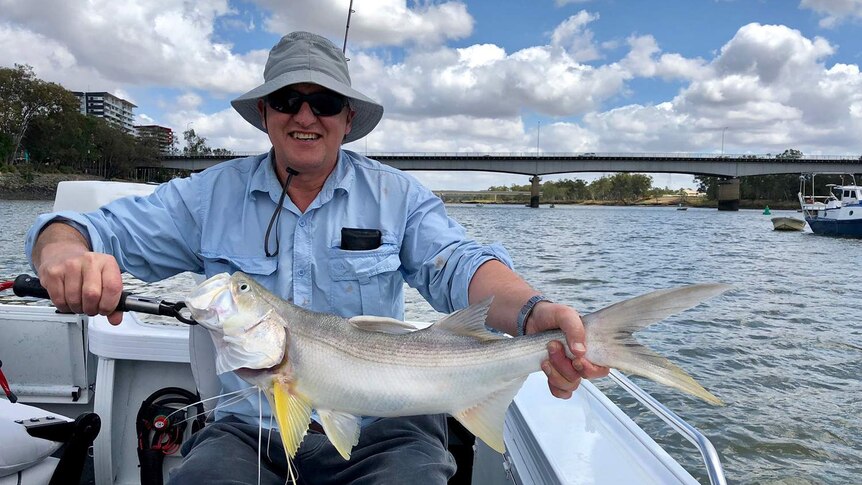 Dr Andrew Carll, wearing a hat and sunglasses, smiles as he sits on a boat in the Fitzroy River in Rockhampton.